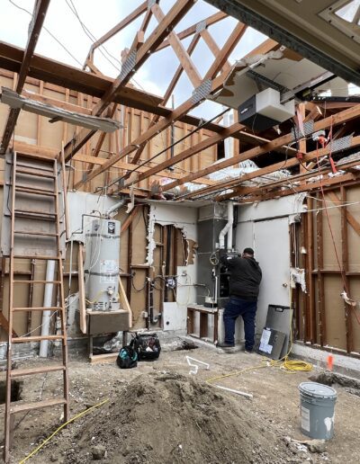 Construction site inside a building with exposed wooden beams and walls. Several workers are present, and various tools and equipment are scattered on the ground. The roof is partially missing.